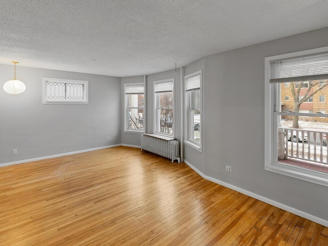 unfurnished room with radiator, light wood-style floors, baseboards, and a textured ceiling