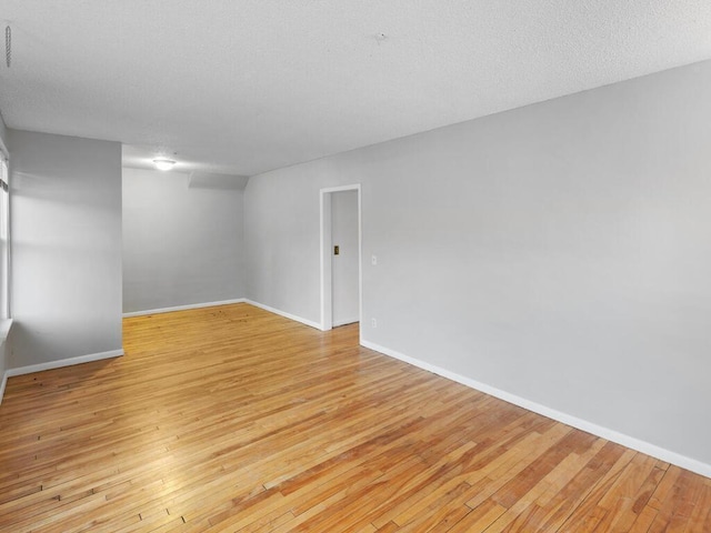 spare room with light wood-style floors, a textured ceiling, and baseboards