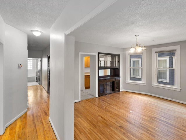 hall featuring light wood finished floors, baseboards, a chandelier, and a textured ceiling