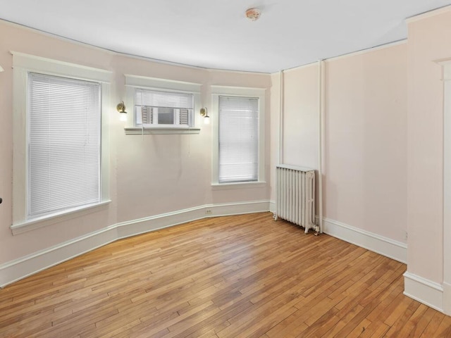 unfurnished room featuring radiator, baseboards, and light wood finished floors