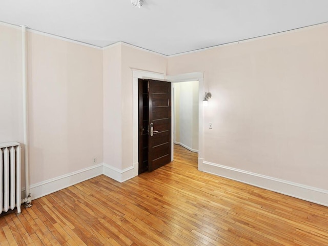 spare room featuring baseboards, light wood finished floors, and radiator heating unit