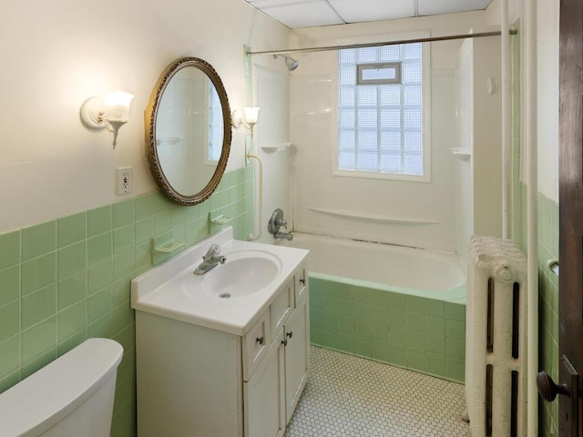 bathroom with radiator, toilet, tiled shower / bath combo, vanity, and tile walls