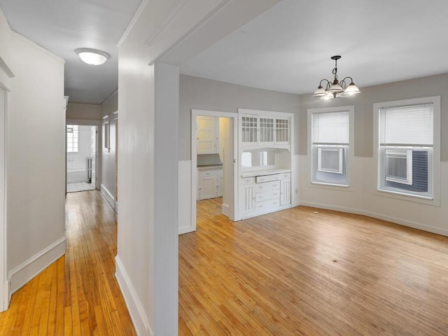 unfurnished dining area featuring light wood-type flooring, baseboards, and a chandelier