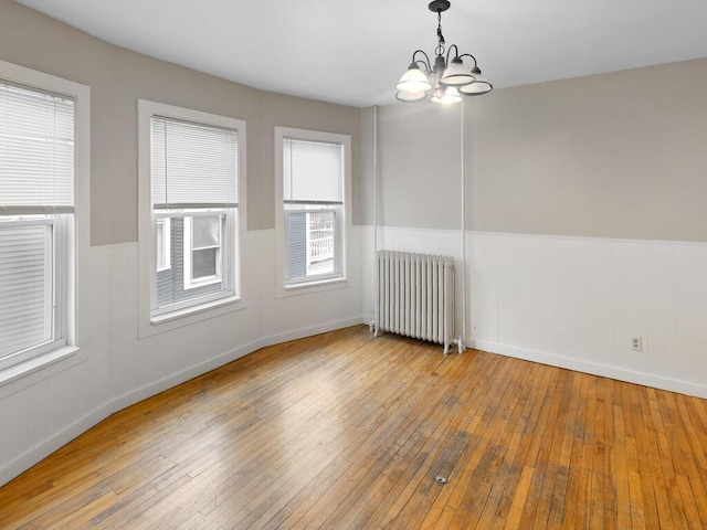 empty room featuring hardwood / wood-style flooring, radiator heating unit, a chandelier, and wainscoting