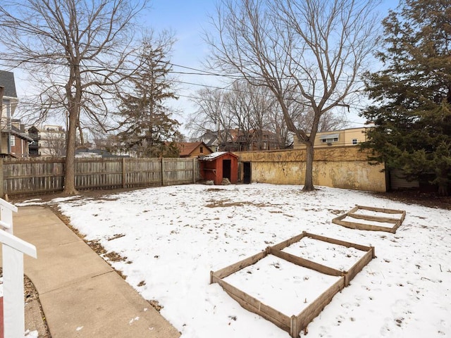 yard layered in snow featuring an outbuilding, a shed, and a fenced backyard