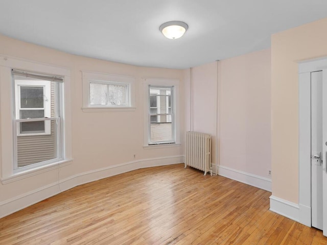 empty room featuring baseboards, light wood-style floors, and radiator