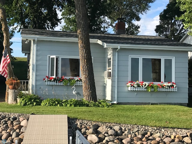 view of side of home with a lawn, a chimney, and roof with shingles