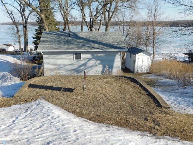 view of snow covered exterior featuring an outbuilding, a storage unit, and roof with shingles