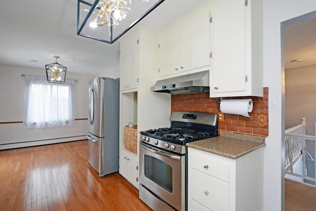 kitchen with light wood-style flooring, under cabinet range hood, white cabinets, appliances with stainless steel finishes, and decorative backsplash