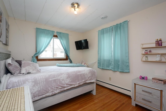 bedroom with a baseboard heating unit and wood finished floors