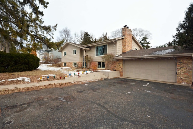 raised ranch with a garage, brick siding, driveway, and a chimney