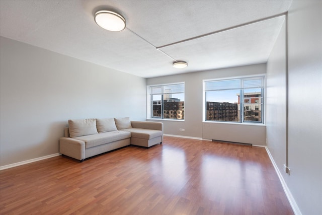 unfurnished living room featuring a textured ceiling, wood finished floors, and baseboards