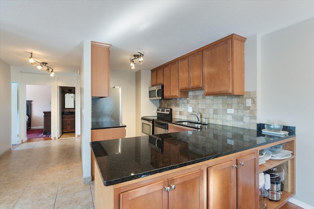 kitchen with light tile patterned floors, appliances with stainless steel finishes, a peninsula, a sink, and backsplash