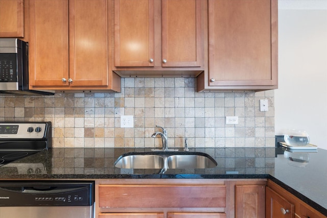 kitchen featuring tasteful backsplash, brown cabinetry, dark stone counters, appliances with stainless steel finishes, and a sink