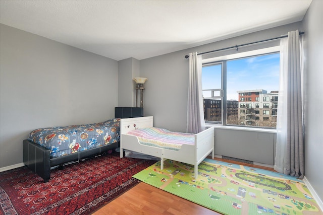 bedroom featuring a view of city, wood finished floors, and baseboards