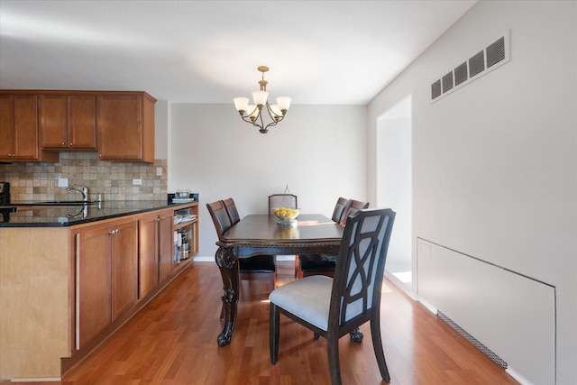 dining room with light wood finished floors, baseboards, visible vents, and a notable chandelier