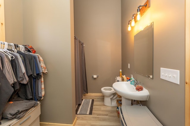 bathroom with toilet, a shower with shower curtain, wood finished floors, a sink, and baseboards