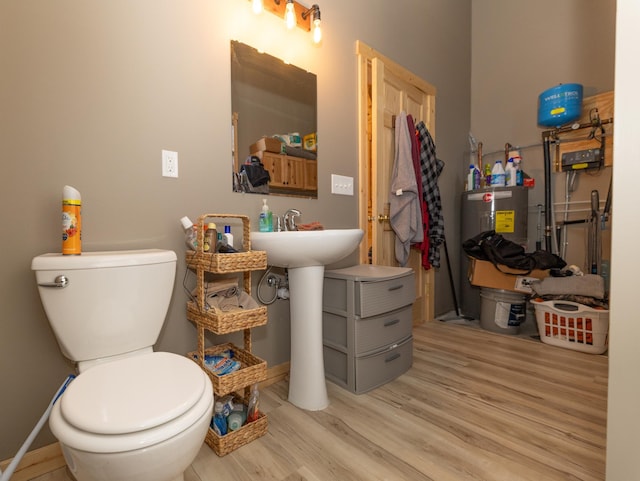 half bathroom with water heater, wood finished floors, toilet, and baseboards