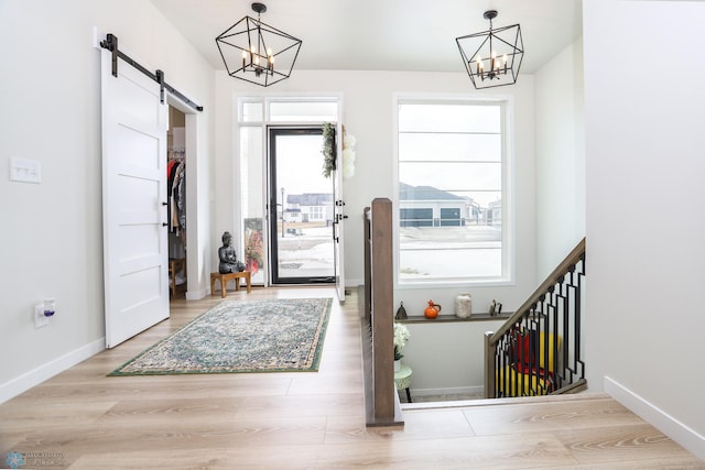 entrance foyer with wood finished floors, a notable chandelier, baseboards, and a barn door