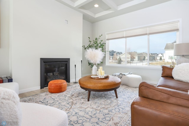 living area with beam ceiling, a glass covered fireplace, wood finished floors, coffered ceiling, and baseboards