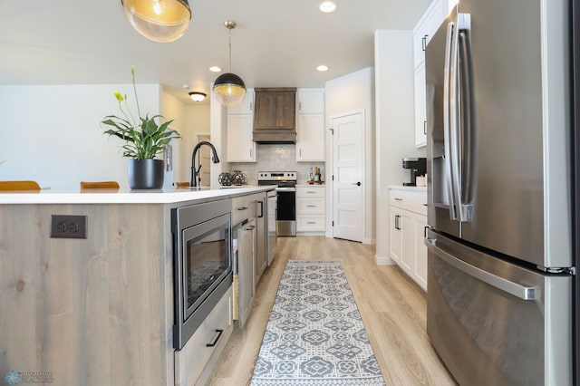 kitchen with white cabinets, light countertops, appliances with stainless steel finishes, decorative backsplash, and light wood finished floors