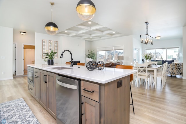 kitchen featuring a center island with sink, light wood finished floors, stainless steel appliances, a sink, and coffered ceiling