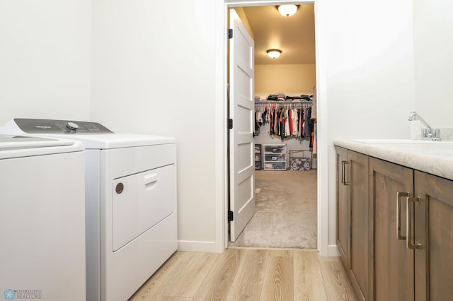 laundry room featuring cabinet space, light colored carpet, light wood-style floors, washing machine and dryer, and a sink