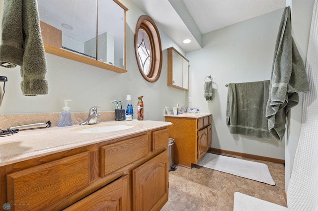 full bathroom featuring a shower, two vanities, a sink, and baseboards