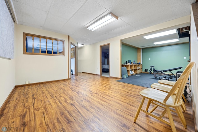 exercise room with wood finished floors, a paneled ceiling, and baseboards