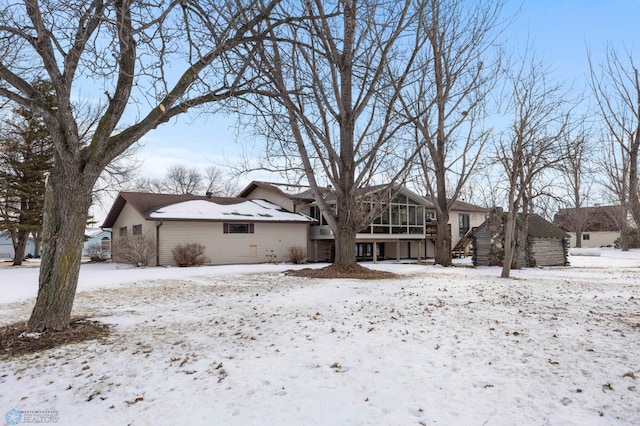 snow covered back of property featuring a garage and a sunroom