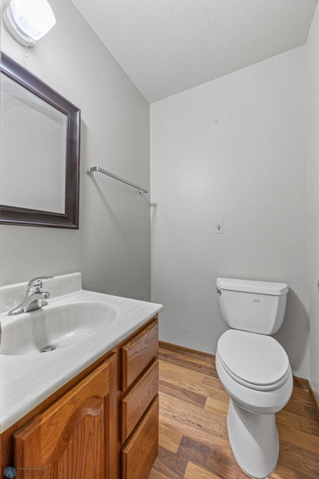 289 2nd St SW, Forman, ND 58032 - half bath with wood finished floors, vanity, toilet, a textured ceiling, and baseboards