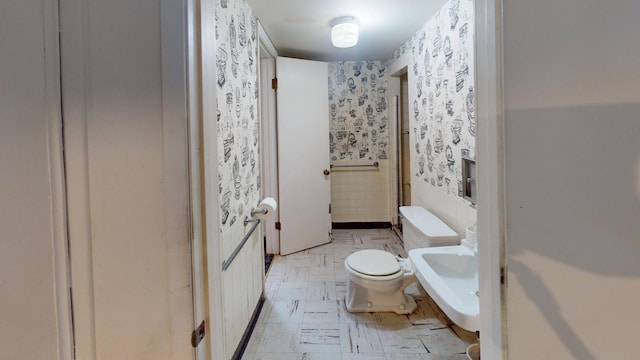 bathroom with wallpapered walls, tile walls, toilet, and a sink