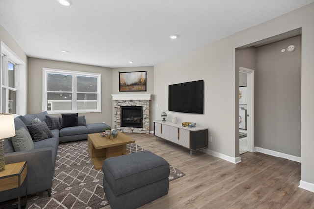 living room with a stone fireplace, recessed lighting, wood finished floors, baseboards, and washer / dryer