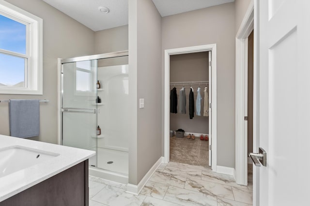 full bathroom featuring marble finish floor, a stall shower, a walk in closet, and baseboards