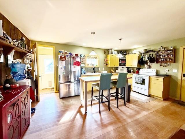 kitchen featuring white electric range, light countertops, light wood-type flooring, freestanding refrigerator, and a center island