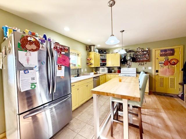 kitchen featuring pendant lighting, stainless steel appliances, cream cabinetry, light countertops, and open shelves