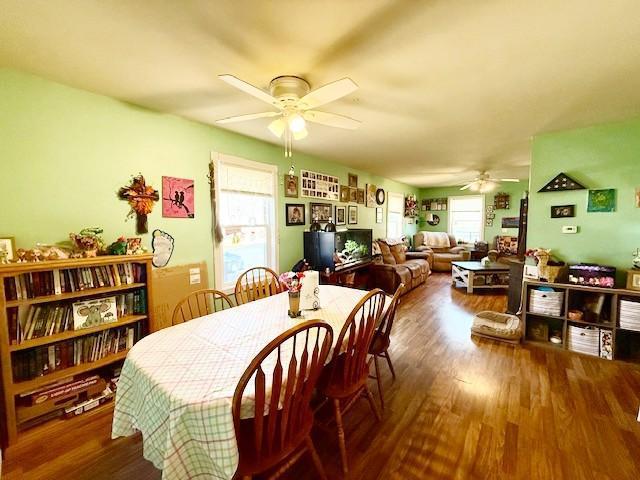 dining space with a ceiling fan, a wood stove, and wood finished floors