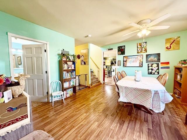 dining space featuring a ceiling fan, wood finished floors, and stairs