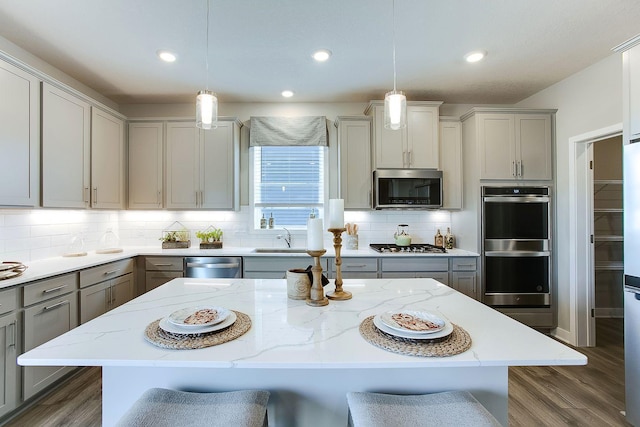 kitchen with decorative backsplash, gray cabinetry, appliances with stainless steel finishes, a sink, and a kitchen bar