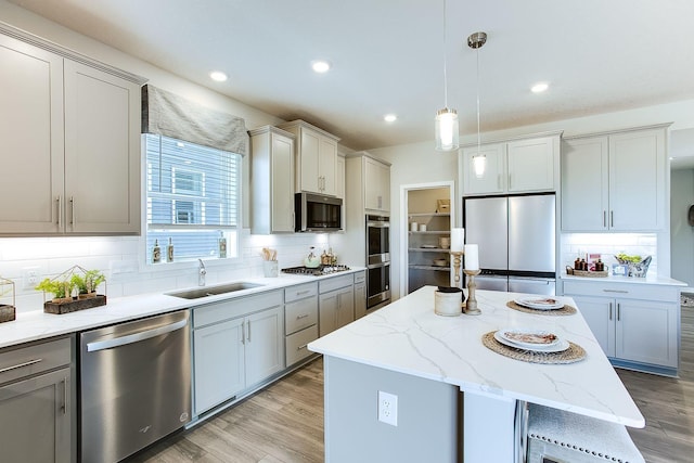 kitchen with a center island, hanging light fixtures, stainless steel appliances, light wood-style floors, and a sink