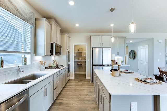 kitchen with stainless steel appliances, a kitchen island, a sink, light wood-type flooring, and tasteful backsplash