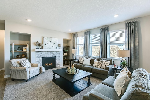 living area with baseboards, a textured ceiling, a stone fireplace, built in shelves, and recessed lighting