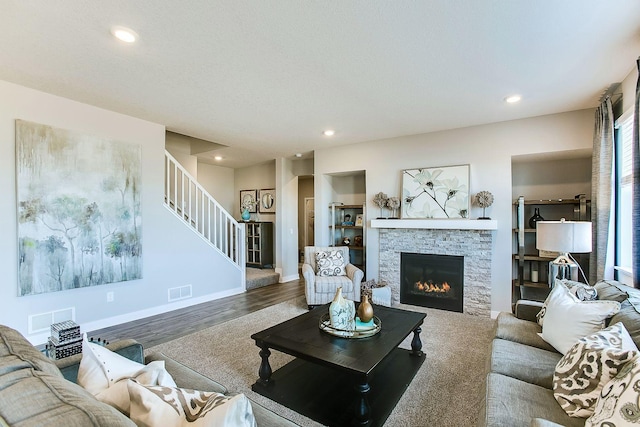 living room featuring a stone fireplace, stairway, visible vents, and recessed lighting