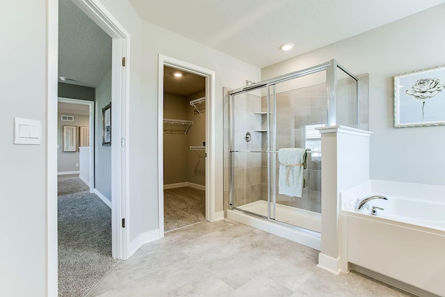 bathroom with a stall shower, a garden tub, a walk in closet, and a textured ceiling