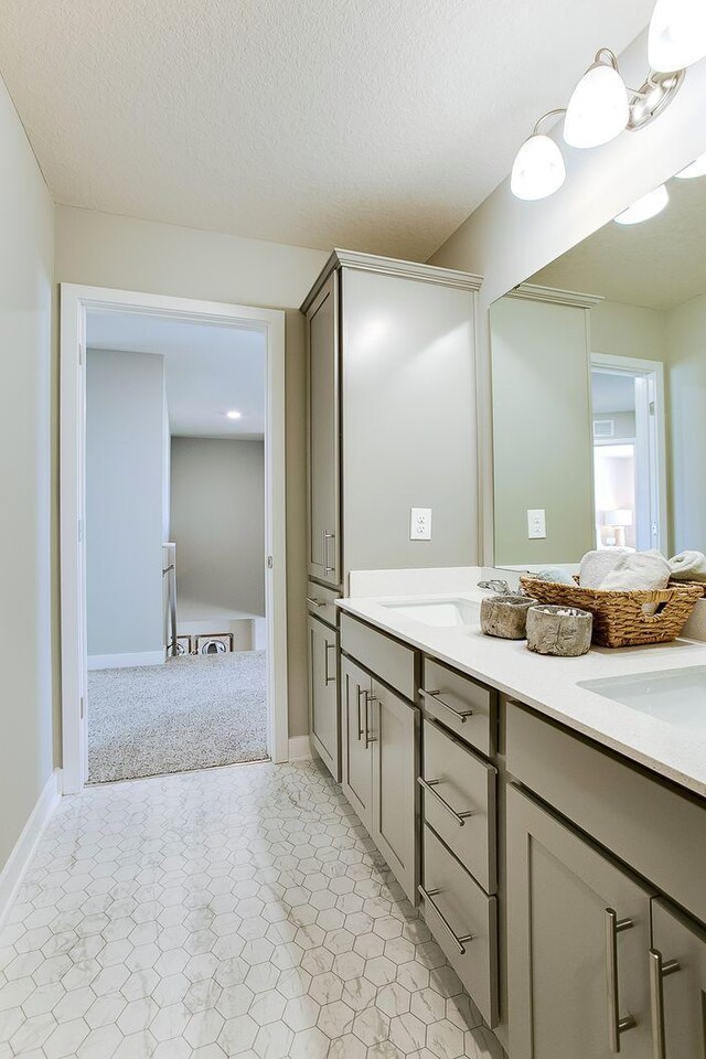 full bath featuring a sink, a textured ceiling, baseboards, and double vanity