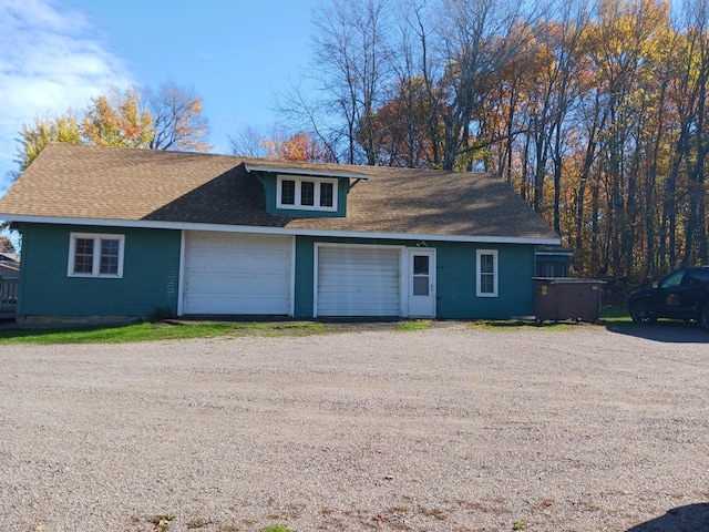 exterior space with an attached garage, a shingled roof, and dirt driveway