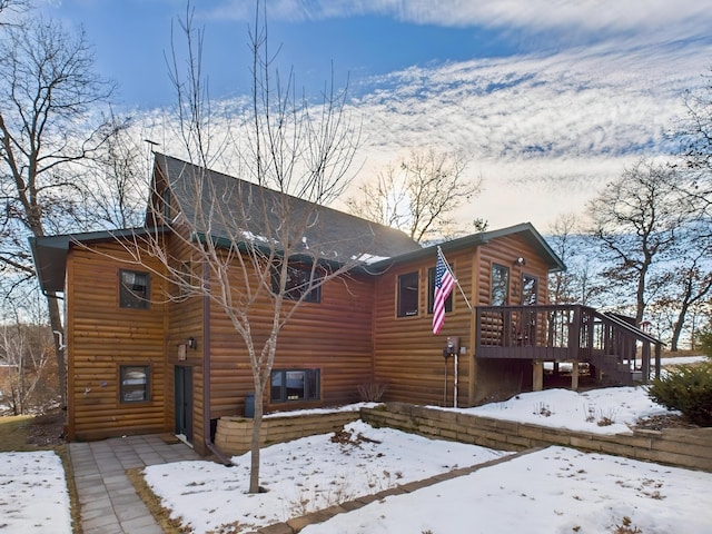 snow covered back of property with a wooden deck and faux log siding