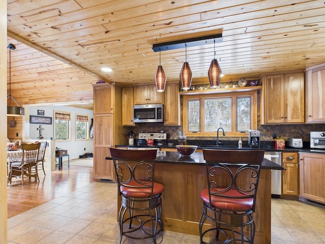 kitchen featuring stainless steel appliances, a kitchen breakfast bar, a center island, tasteful backsplash, and dark countertops