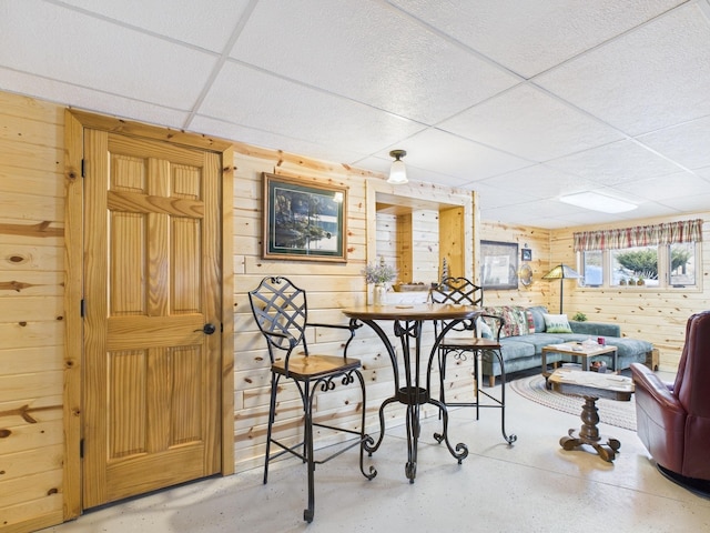 dining area with concrete floors, a drop ceiling, and wooden walls