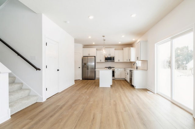 kitchen featuring light wood-style flooring, white cabinets, light countertops, appliances with stainless steel finishes, and decorative backsplash